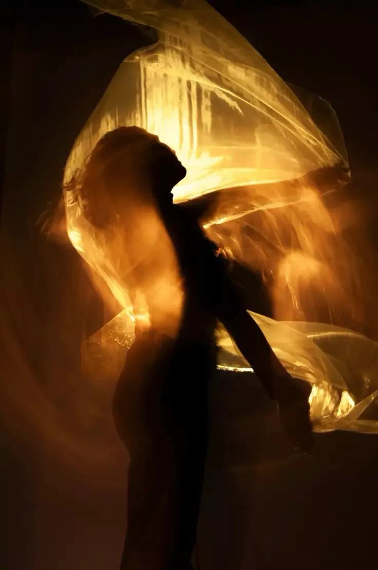 A woman bathed in golden light, wrapped in flowing translucent fabric